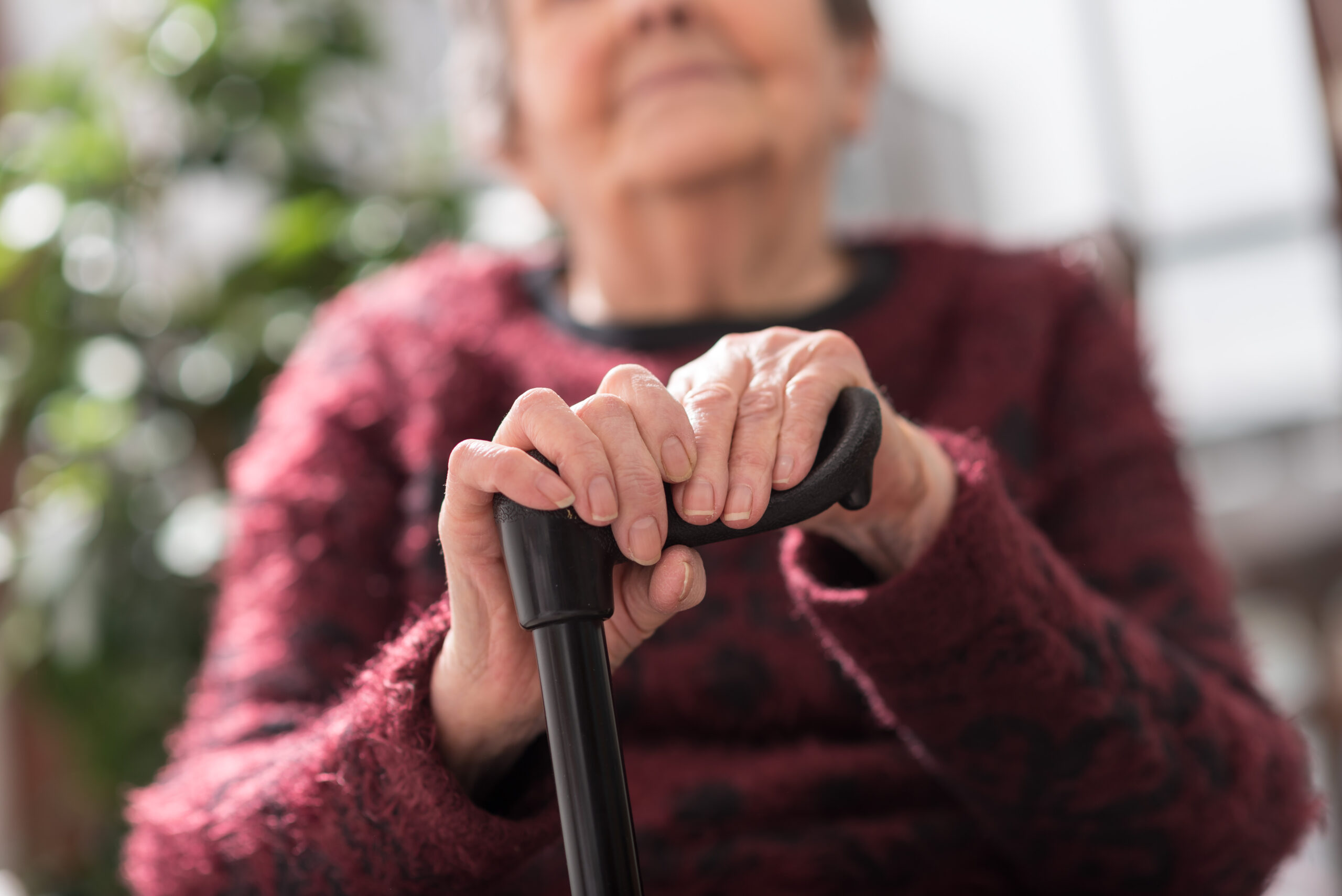 Old woman sitting with her hands on a cane