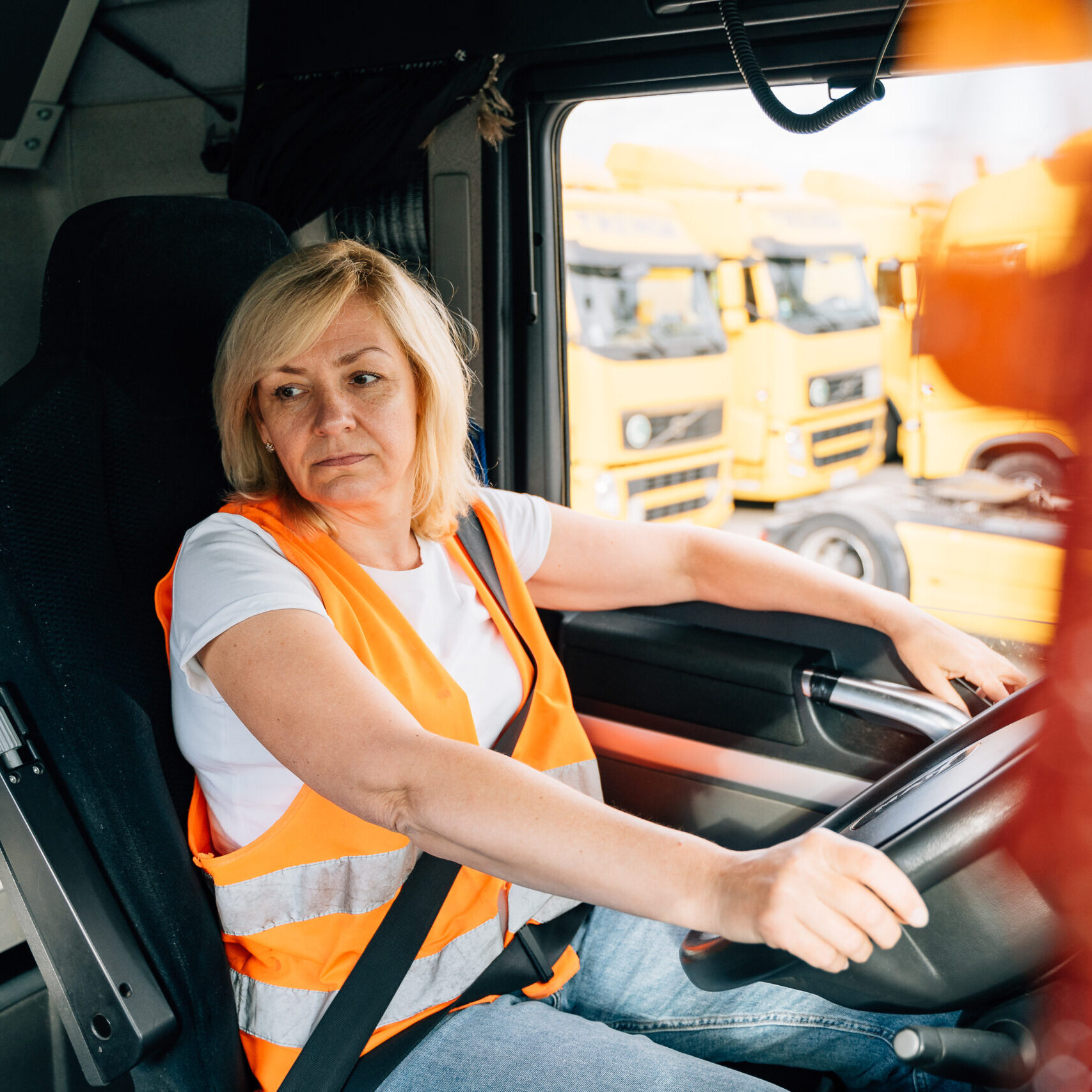 Mature woman truck driver steering wheel inside lorry cabin.